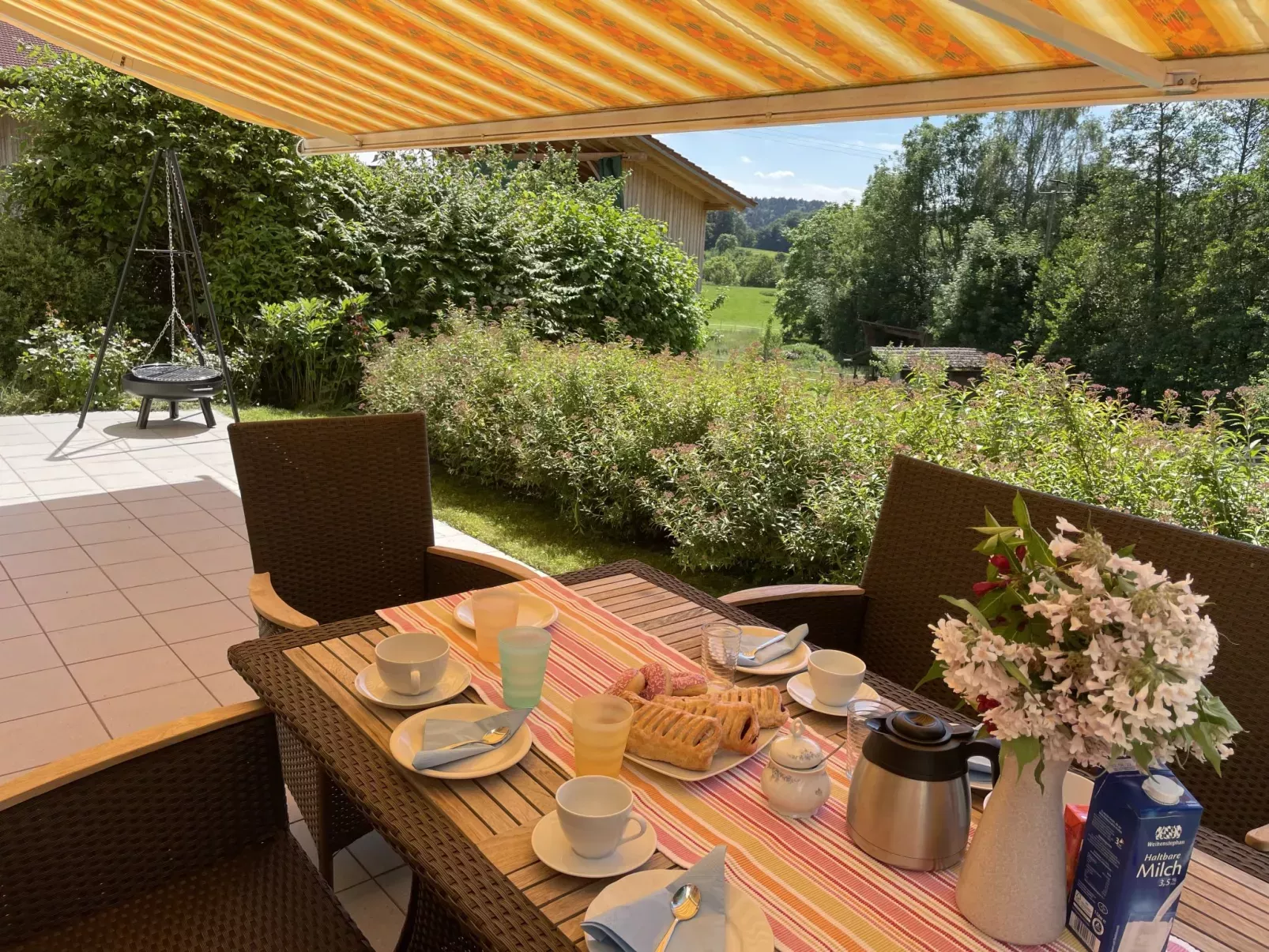 tuinset onder een zonnedoek, met gedekte tafel, bloemen op tafel en 2 stoelen in tuin bij vakantiehuis SuB