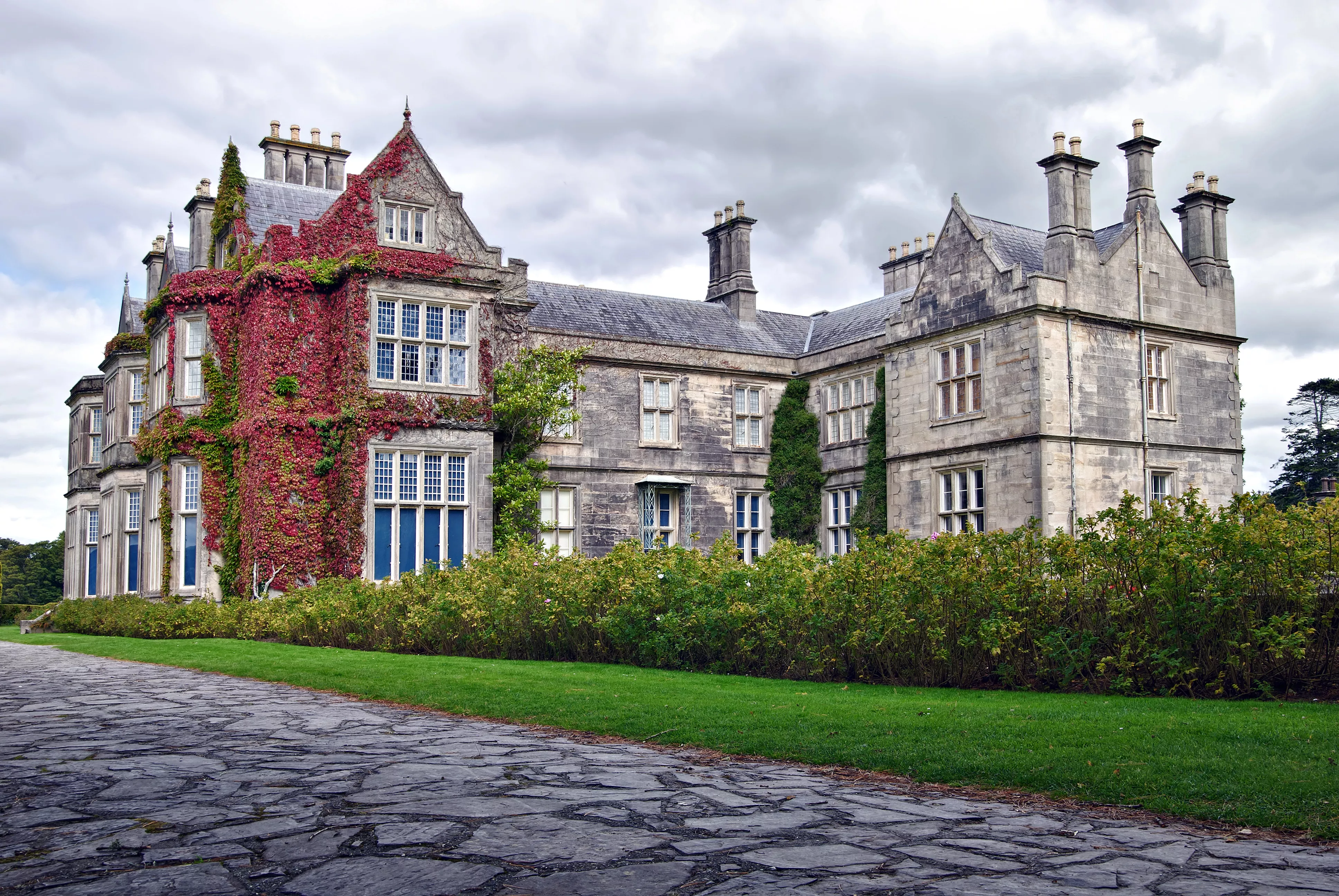 Victoriaans landhuis Muckross House met klimplanten aan de gevel en een stenen pad op de voorgrond.